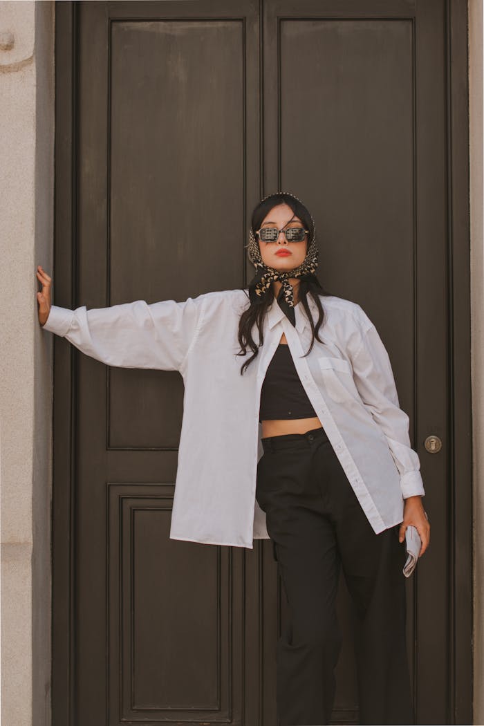 Stylish woman in a headscarf and sunglasses poses against a classic wooden door, exuding elegance.